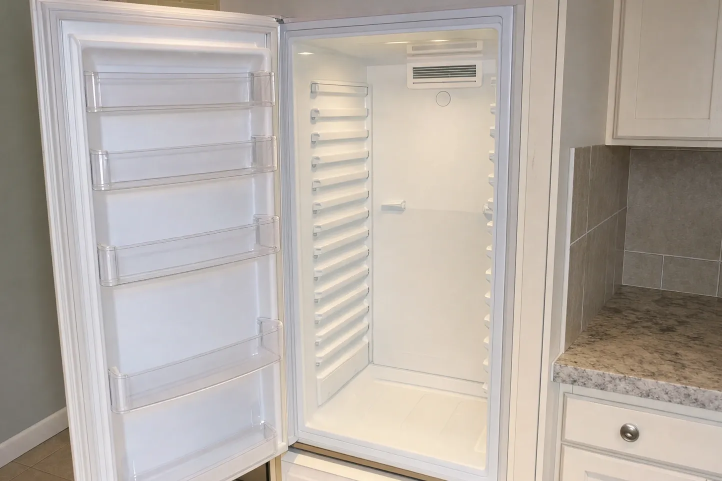 Full-height refrigerator column with the door wide open, shelves removed and the rear air vent visible